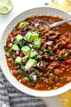 a white bowl filled with chili, beans and avocado next to tortilla chips