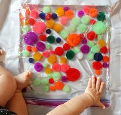 a baby laying on top of a bed next to a plastic bag filled with pom poms