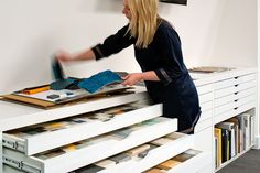 a woman in black shirt and blue gloves working on some drawers with bookshelves