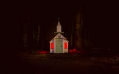 a small white church in the dark with red light coming from it's windows