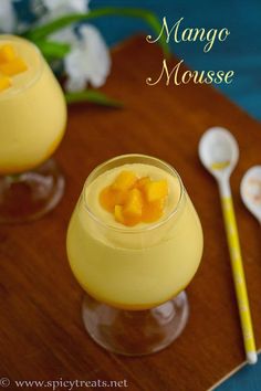 mango mousse in small glasses with spoons and flowers behind them on a wooden tray