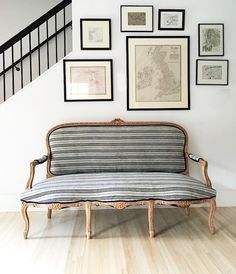 a couch sitting under a stair case next to a wall with framed pictures on it