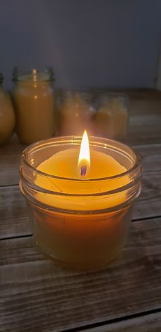 a lit candle sitting in a glass bowl on a wooden table with jars behind it