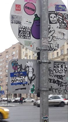 a street sign covered in stickers on the side of a road with cars passing by