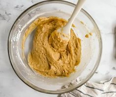 a mixing bowl filled with peanut butter next to a wooden spatula on top of a marble counter