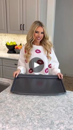 a woman standing in front of a kitchen counter holding a tray with lipstick on it