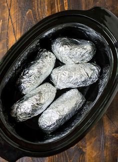 foil wrapped burritos in a slow cooker on a wooden table with tongs