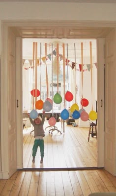 a young boy standing in front of a doorway with balloons hanging from it's ceiling