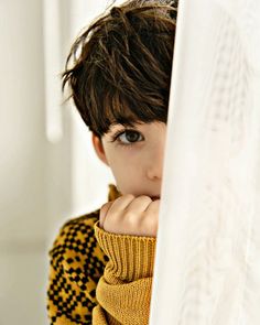 a young boy is peeking out from behind a curtain