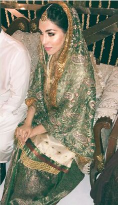 a woman sitting on top of a bed wearing a green and gold wedding dress,