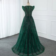 a green evening gown on display in front of a white wall with curtains and drapes