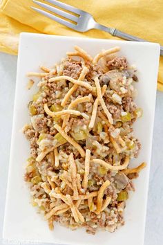 a white plate topped with rice covered in ground beef and veggies next to a fork