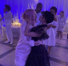 two girls in wedding dresses hugging each other at a party with purple lighting behind them