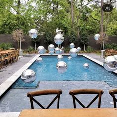 an outdoor pool with large silver balls floating in the water and wooden chairs around it