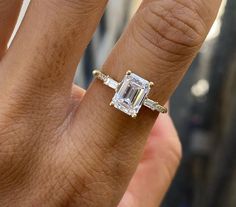 a woman's engagement ring with an emerald and diamond set in the middle, on her finger