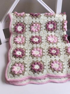 a crocheted blanket with pink and white flowers on it sitting on a chair