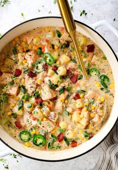 a pot filled with chicken and vegetables next to a gold spoon on top of a table