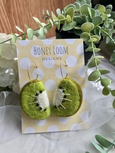 a pair of green and white earrings sitting on top of a table next to flowers