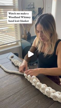 a woman is making something out of yarn on a table with the caption, watch me make a woodland whimsy hand knitt blanket