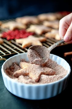 a person scooping sugar into a bowl with cookies in the background on a cooling rack