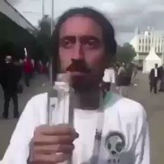 a man holding up a glass bottle with something in it's mouth while standing on the street