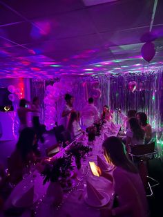 a group of people sitting around a table in a room with purple lights and streamers