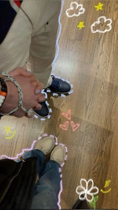 two people standing next to each other on top of a wooden floor with colorful chalk drawings