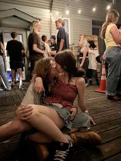 two women sitting on the ground kissing while others are standing around in the back yard