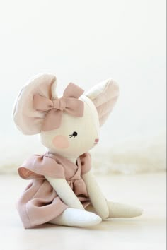 a small stuffed animal with a pink dress and bow on it's head sitting on the floor