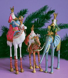 three colorful figurines are standing next to a christmas tree on a purple surface