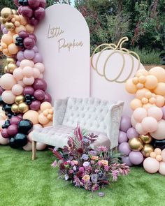 a couch sitting on top of a lush green field next to a bunch of balloons