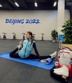 a woman sitting on a blue mat in a gym