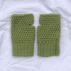 two green crocheted mittens sitting on top of a white cloth covered table