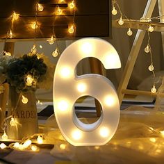 the number six is lit up with fairy lights in front of a bed and dresser