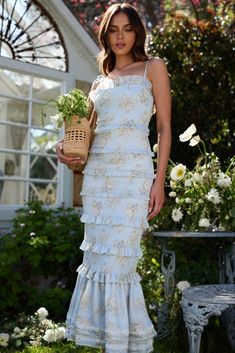 a woman in a white dress holding a basket with flowers on it and posing for the camera