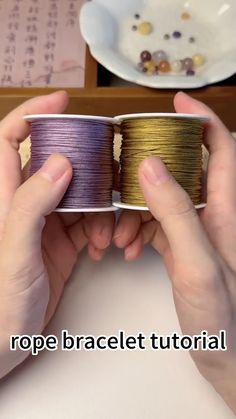 two hands holding different colored spools of thread in front of a plate and bowl