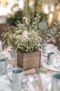 a wooden box filled with lots of flowers on top of a table covered in plates and cups