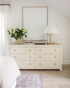 a bedroom with a dresser, lamp and flowers on top of it in front of a large mirror