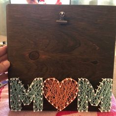 the word mom spelled with string art in front of a wooden box on a table