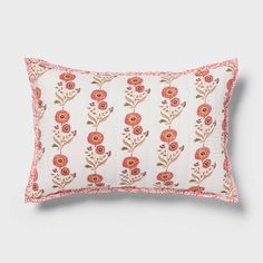 a white pillow with pink and red flowers on the front, sitting against a gray background