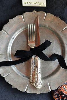 a silver plate with a black ribbon on it next to a fork and knife that is sitting on a table