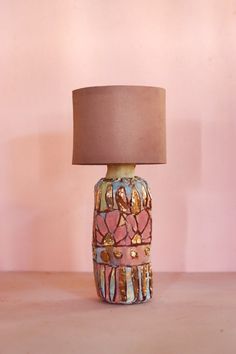 a ceramic lamp sitting on top of a wooden table next to a pink wall with a brown lampshade