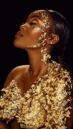 a woman with gold paint on her face and body, looking up at the sky