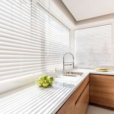 a kitchen with wooden cabinets and white counter tops next to a window covered in blinds