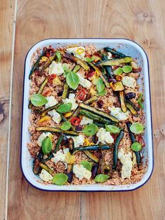 a casserole dish filled with vegetables and rice on a wooden table next to a fork