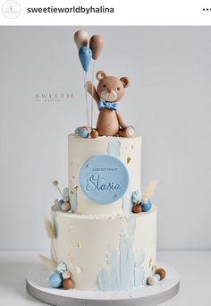 a three tiered cake with a teddy bear on top and balloons in the air