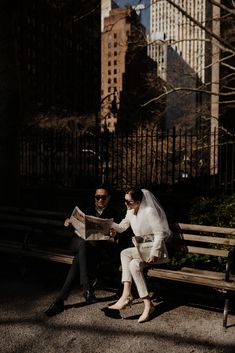 a bride and groom are sitting on a bench in the middle of new york city