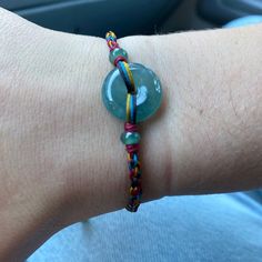 a person's arm with a bracelet made out of glass beads and multicolored cords