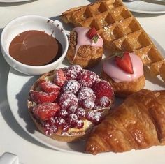 a white plate topped with waffles, strawberries and other desserts next to a cup of chocolate