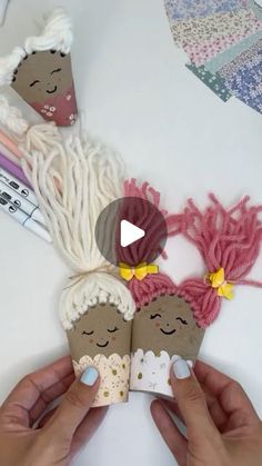 someone is holding two small paper dolls with yarn on the table next to other crafting supplies